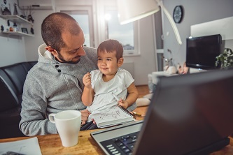 Man working from home in front of laptop while nursing his young son