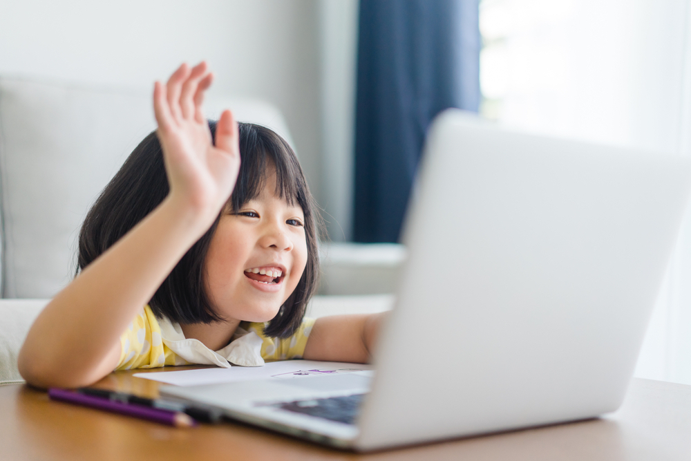 Photograph of a young child with black hair waving to a computer indicating that they are currently online and that COPPA compliance is required.